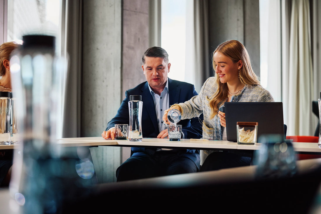 Two professionals sitting at a table and pouring water from into a glass.